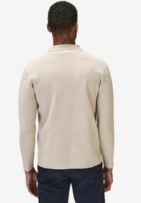 Beige långärmad polo skjorta med texturerad stickning och krage. Sömmen är något rundad, vilket ger en avslappnad silhuett.