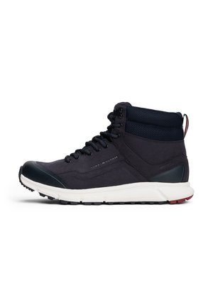 Zwarte hoge sneaker met gevoerde enkelkraag, veters aan de voorkant, witte zool en Tommy Hilfiger-logo aan de zijkant.