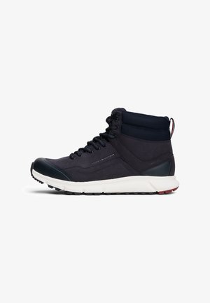 Czarny sneaker z wysoką cholewką, wyściełanym kołnierzem na kostkę, sznurowaniem z przodu, białą podeszwą i logo Tommy Hilfiger po boku.