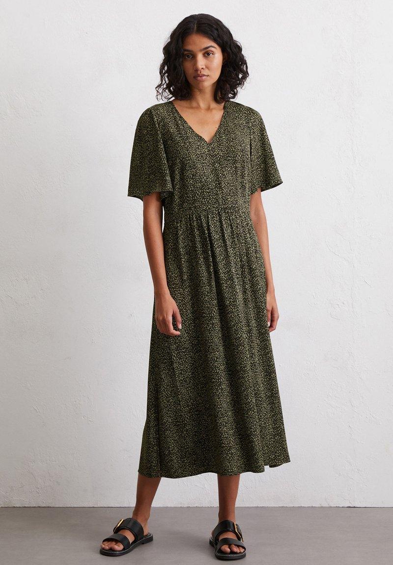 Green patterned dress with a v-neckline, short flutter sleeves, and a flowy silhouette. Worn with black flat sandals. Fabric appears lightweight.