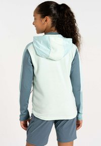 Helleblaue Fleece-Hoodie mit einer glatten Kapuze, langen dunkelblauen Ärmeln und einer Reißverschlusstasche an der Seite. Getragen mit grauen Shorts.