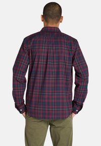 Camisa de cuadros de manga larga en tonos azul marino, rojo y amarillo; presenta puños con botones y un diseño de yugo en la parte posterior. Hecha de tejido hecho a máquina.