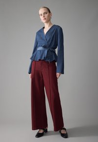 Blusa avvolgente blu scuro con orlo peplum, abbinata a pantaloni a gamba larga bordeaux a vita alta. Completata con scarpe con tacco a blocco nere.