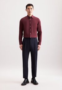 Camicia button-up a maniche lunghe di colore bordeaux abbinata a pantaloni eleganti blu navy e scarpe in pelle nera. Tessuto morbido, colletto classico e vestibilità dritta.