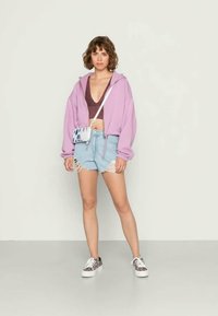 Hoodie cropped roxa, top cropped castanho e calções de ganga claros com bordas desfiadas. Finalizado com ténis estampados e uma pequena mala de crossbody.