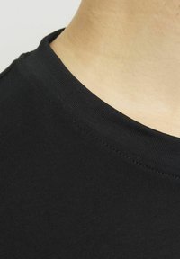Černé bavlněné tričko s límcem, který ukazuje hladkou texturu a detailní záběr na šev u krku, s čistým, zaobleným výstřihem a bez dalších ozdob.