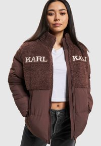 Brun pufferjakke med en tekstureret fleece-overdel, med "KARL" broderi i cremefarve på begge sider, lynlåslukning og sidelommer.