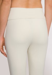 Leggings a vita alta in morbido tessuto color crema chiaro con una texture liscia. Presentano un logo sottile in vita e una silhouette aderente.