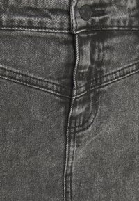 Jeans in denim grigio con un design classico a cinque tasche, cuciture resistenti e una chiusura con bottone in metallo in vita. Texture sottile visibile.