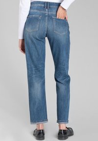 Jean en denim bleu clair avec une coupe droite, cinq poches et des ourlets retroussés. Le tissu présente des détails de décoloration subtile et d'usure.