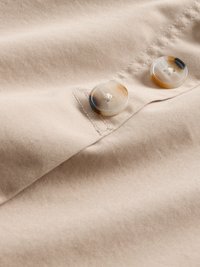 Beige stoff med en glatt tekstur har to sirkulære knapper i nyanser av beige med et marmorert mønster, plassert ved sømmen.