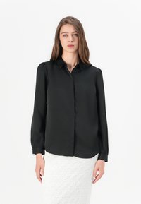 Zwarte blouse met lange mouwen en een kraag, met een gladde textuur en een knoopsluiting aan de voorkant. Voorzien van subtiele pofmouwen en een getailleerde pasvorm.