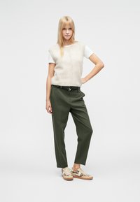 Bézs kötött ujjatlan pulóver fehér inggel, zöld szabott nadrág és mintás bézs sportcipő. Egyszerű kialakítás finom textúrákkal.