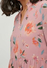 Robe fleurie rose clair avec des fleurs orange et bleu sarcelle, dotée d'un décolleté en V et d'un tissu doux ; taille froncée avec une jupe fluide.