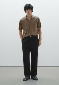 Polo shirt marrone a maniche corte con una texture morbida, abbinato a pantaloni neri a gamba larga e sandali neri intrecciati. Design minimale, senza motivi.