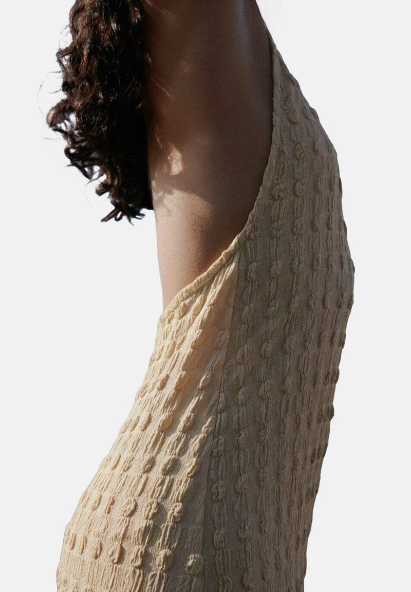 Hellbeiges Kleid aus strukturiertem Stoff mit erhöhten Knoten, ärmellos und mit schwingendem Schnitt. Geschmeidiges, weiches Material.
