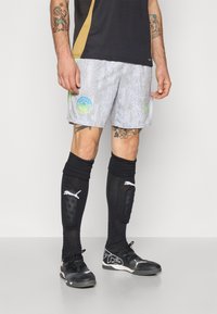 Grå shorts med et vanddråbe mønster og et blåt logo. Sorte knæsokker med hvid branding. Sorte sportsko med et struktureret design.