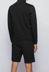 Felpa nera con colletto alto, maniche lunghe e pantaloni corti abbinati. Tessuto morbido, design semplice e polsini e orlo a coste.