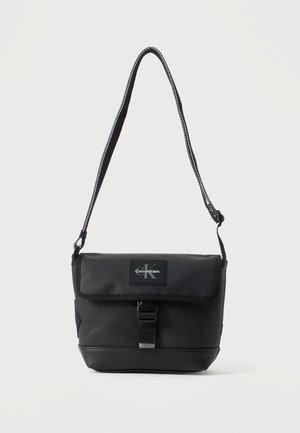 Czarna torba na ramię Calvin Klein z regulowanym paskiem, przednią klapą, zapięciem na klamrę i widoczną naszywką z logo marki.