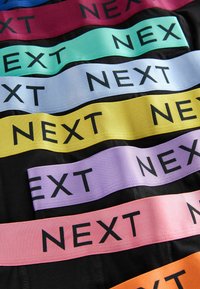 Večbarvni elastični trakovi s tiskom "NEXT" v črni barvi. Barve vključujejo rdečo, teal, modro, rumeno, vijolično, roza in oranžno na črnem blagu.