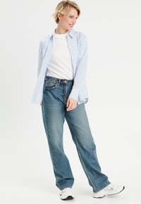 Chemise à boutons avec des rayures bleu clair et blanches, associée à un jean bleu taille haute et ample et des baskets blanches. Tissu lisse, coupe décontractée.