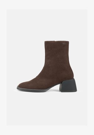 Brown suede ankle boot with a pointed toe and a thick black heel; features a smooth texture and a zip closure on the side.