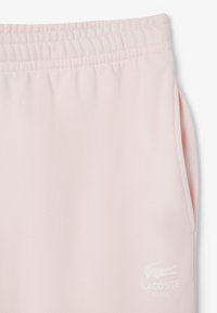 Lichtroze sweatsbroek van zacht materiaal, met een elastische taille, zijzakken en een klein wit Lacoste-logo bij de zoom.