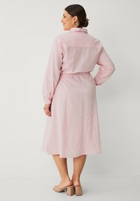 Lichtroze midi-jurk met een kraag, lange mouwen, elastische taille en zijsplitsen. Gemaakt van zachte stof; heeft gathered details.