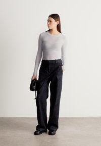 Svetlo siva rebrasta majica z dolgimi rokavi, visokim pasom temne denim hlače, črna torbica z vrvico, črni ploski čevlji, minimalističen dizajn.