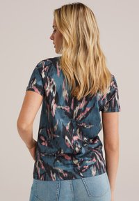 T-shirt à manches courtes de couleur bleu foncé avec un motif abstrait vif en rose et crème. Tissu doux et coupe ajustée. Encolure ras du cou simple.