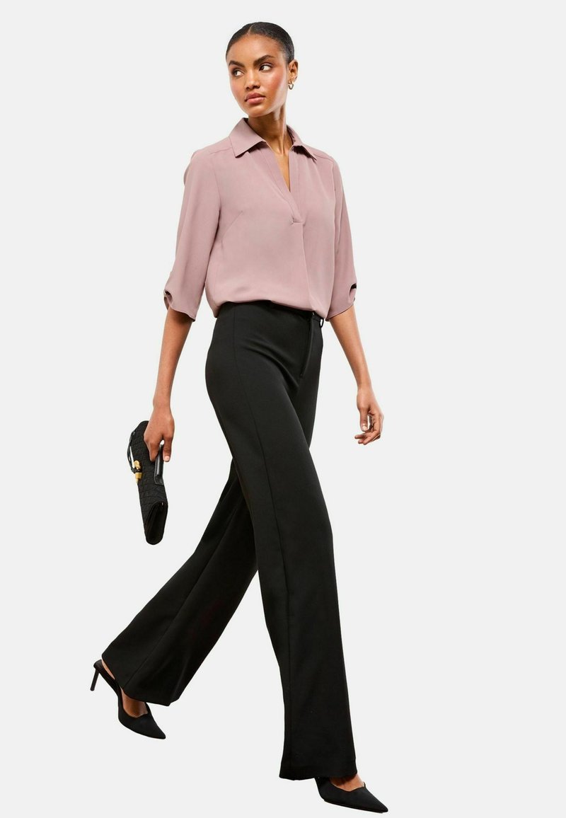Blusa rosa chiaro a maniche corte con colletto; pantaloni neri a vita alta; tacchi neri a punta; porta una pochette nera texture.