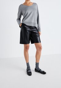 Harmaa neulepaita, mustat keinonahkaiset shortsit, harmaat sukat ja mustat balleriinat valkoisilla niiteillä. Yksinkertainen muotoilu ja rento istuvuus.