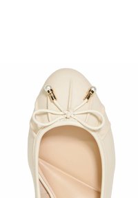 Ballerines en cuir beige avec un bout arrondi, ornées d'un nœud décoratif et de finitions en métal doré, comprenant deux détails qui ressemblent à des perles.