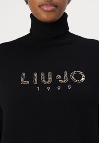 Zwarte coltrui met "LIU•JO" en "1995" versierd met zilveren en gouden strass-steentjes. Zachte stof met een aansluitende pasvorm.