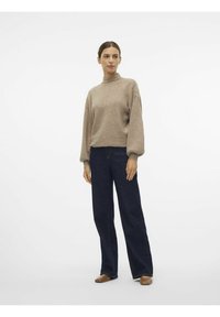 Beige ullblandad tröja med hög hals och ballongärmar, i kombination med mörkblå vida jeans och bruna platta skor.