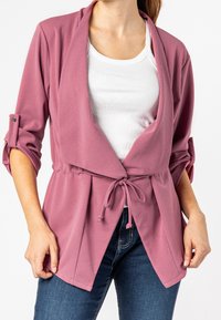 Veste légère mauve avec un design portefeuille, manches longues, poignets retroussés et ceinture à nouer. Présente une texture lisse et une coupe décontractée.