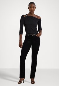 Melnā off-shoulder blūze ar dekoratīvu adatu, apvienota ar melnām samta taisnām biksēm un melnām augstpapēžu sandalēm.