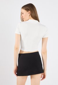Vit, kortärmad, kort polo-top i ribbat material, kombinerad med en svart mini-kjol med rak fåll.