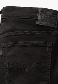 Crne traperice od denima sadrže kožni znak s natpisom "Levi Strauss & Co." i jedinstveni dizajn stražnjeg džepa s dvostrukim šavovima.