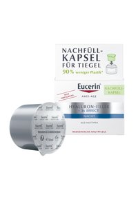 Eucerin night refill capsules in a circular silver container. Packaging labeled green for reduced plastic usage. Text in black and blue.