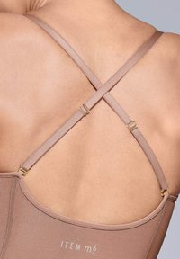 Bruine bodysuit met kruislingse banden, voorzien van gouden hardware-accenten en een gladde textuur, die minimalistische designelementen benadrukt.