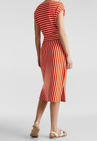 Czerwona i biała sukienka w paski z dopasowanym gorsetem, rozkloszowanym dołem i rozcięciem z tyłu. Wykonana z miękkiego, elastycznego materiału.