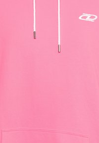 Růžová mikina s kapucí z měkké látky, s přední kapsou, bílými šňůrkami s kovovými koncovkami a malým bílým logem na hrudi.