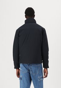 Black puffer jacket with a high collar, smooth texture, and minimalist design. Includes a logo detail on the back and long sleeves.
