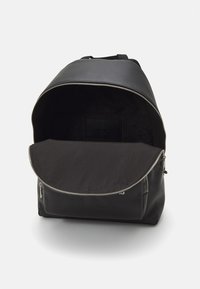 Zaino nero realizzato in pelle liscia con chiusura a zip, dotato di un ampio interno foderato e di un discreto etichetta con logo all'interno.