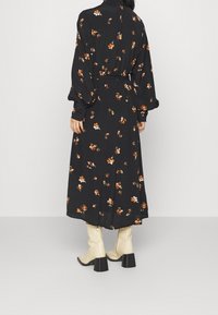 Svart långärmad klänning med blommönster i orange och grön. Har en åtsittande midja och flödande silhuett. Matchas med krämfärgade knähöga stövlar.