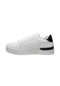 Sneaker bianca con tomaia in sintetico liscia, lacci piatti e un accentuazione nera sul tallone. Presenta una suola bianca spessa con una delicata striscia nera.