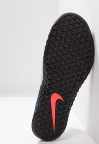 Suela de zapato deportivo Nike en goma negra con un patrón texturizado; presenta un acento de logo rojo y detalles laterales azules.