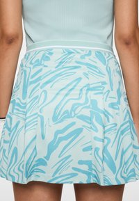 Donna che indossa una minigonna plissettata con motivi astratti azzurri e un top a coste azzurro coordinato, mostrata dalla vita a metà coscia.