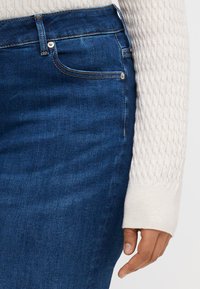 Denim skirt in dark blue with a smooth texture, featuring a standard five-pocket design and metallic hardware accents at the waist.